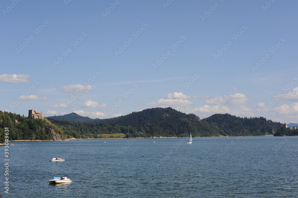 Blue waters of Czorsztyn dam lake with yacht and green hills and mountains and blue sky with clouds in summer in southern Poland Blue waters of Czorsztyn dam lake with yacht and green hills and mountains and blue sky with clouds in summer in southern Poland