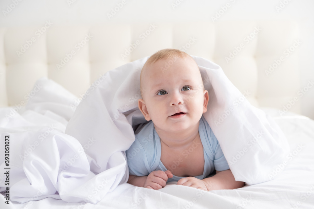 funny baby boy smiling and lying on a white bedding at home. 