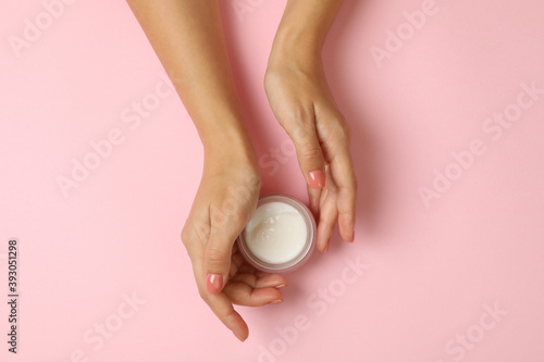 Cute female hands hold jar of cosmetic cream on pink background