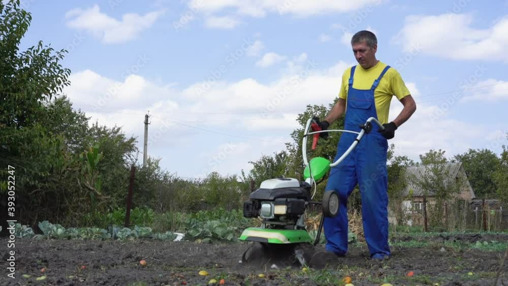 Man cultivates the ground in the garden with a tiller, preparing the soil for sowing Man cultivates the ground in the garden with a tiller, preparing the soil for sowing