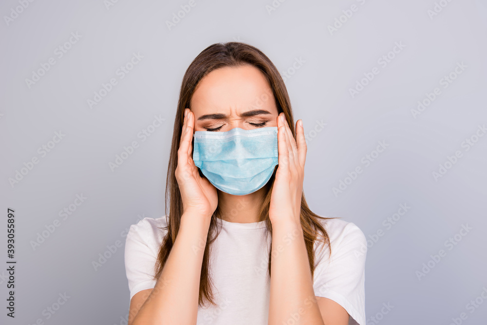 Photo portrait of girl with headache touching temples wearing blue face mask isolated on grey colored background Photo portrait of girl with headache touching temples wearing blue face mask isolated on grey colored background