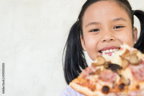 cute little girl holds piece of pizza  feels pleased as spends free time with friends in pizzeria  looks happily directly at camera  wants to eat  wears casual outfit  people and snack concept.