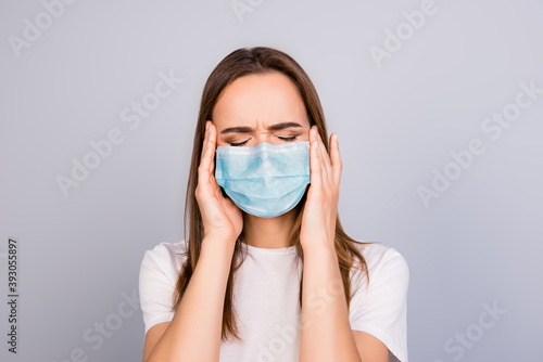 Photo portrait of girl with headache touching temples wearing blue face mask isolated on grey colored background