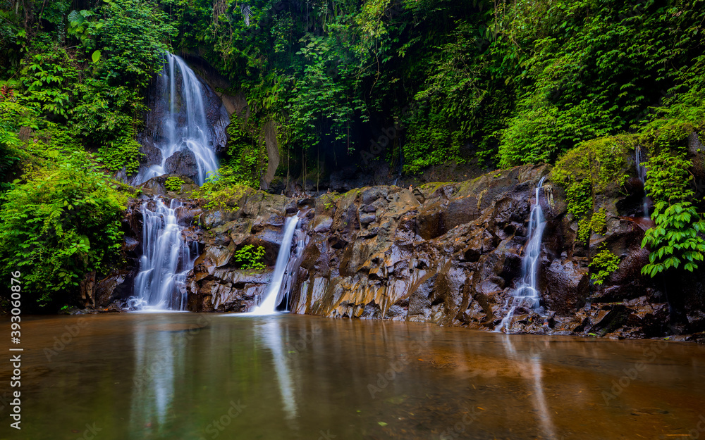 Obraz premium Waterfall landscape. Beautiful hidden Pengibul waterfall in rainforest. Tropical scenery. Water reflection. Slow shutter speed, motion photography. Nature background. Bali, Indonesia