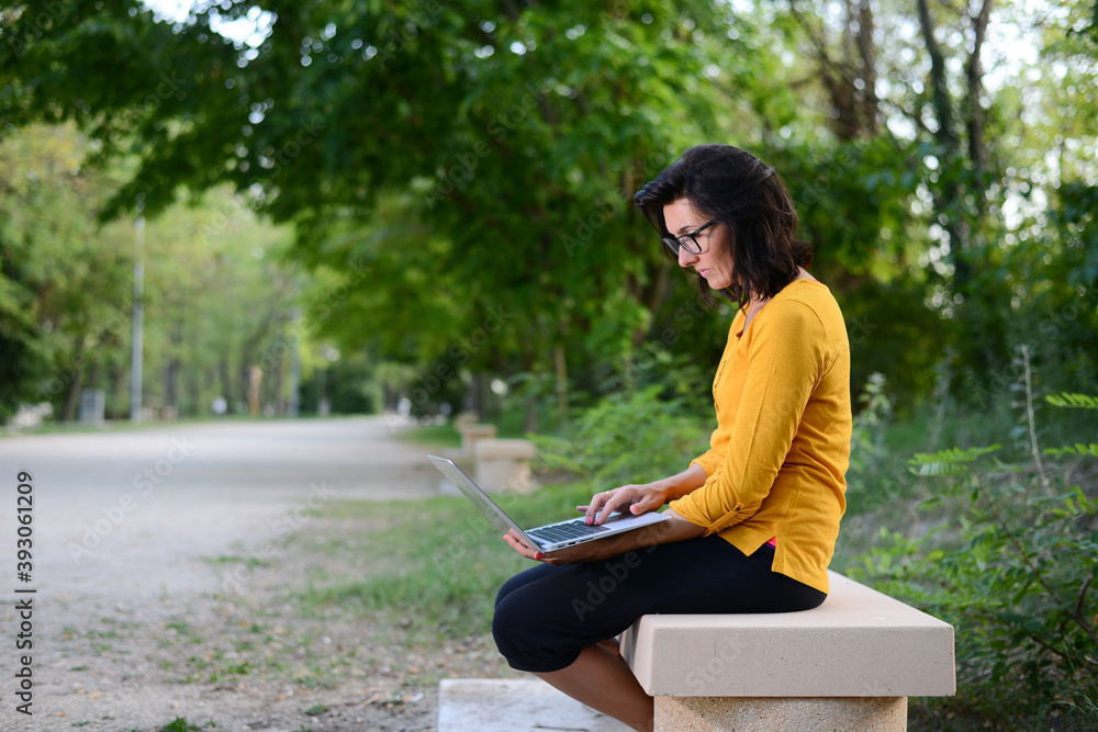 Obraz premium portrait of beautiful and cheerful mature woman working outdoor in a park with wireless connection and a laptop computer
