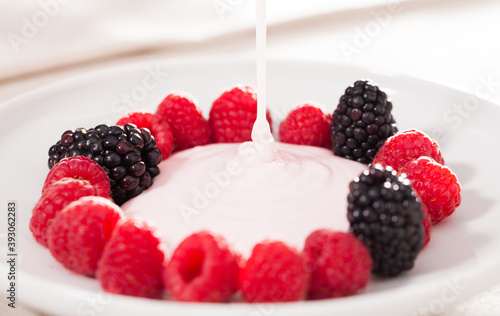 fresh raspberries and blackberries laid out on a white plate in circle with yogurt