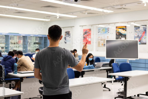 teacher standing or hand with marker while teaching lessons to students in blurred school classroom with a digital blackboard