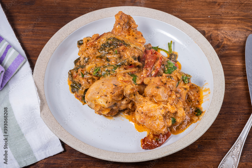 Ready Italian dish - Tuscan chicken with sun-dried tomatoes, tomato paste, spinach, cream and cheese on a plate on a wooden table Ready Italian dish - Tuscan chicken with sun-dried tomatoes, tomato paste, spinach, cream and cheese on a plate on a wooden table