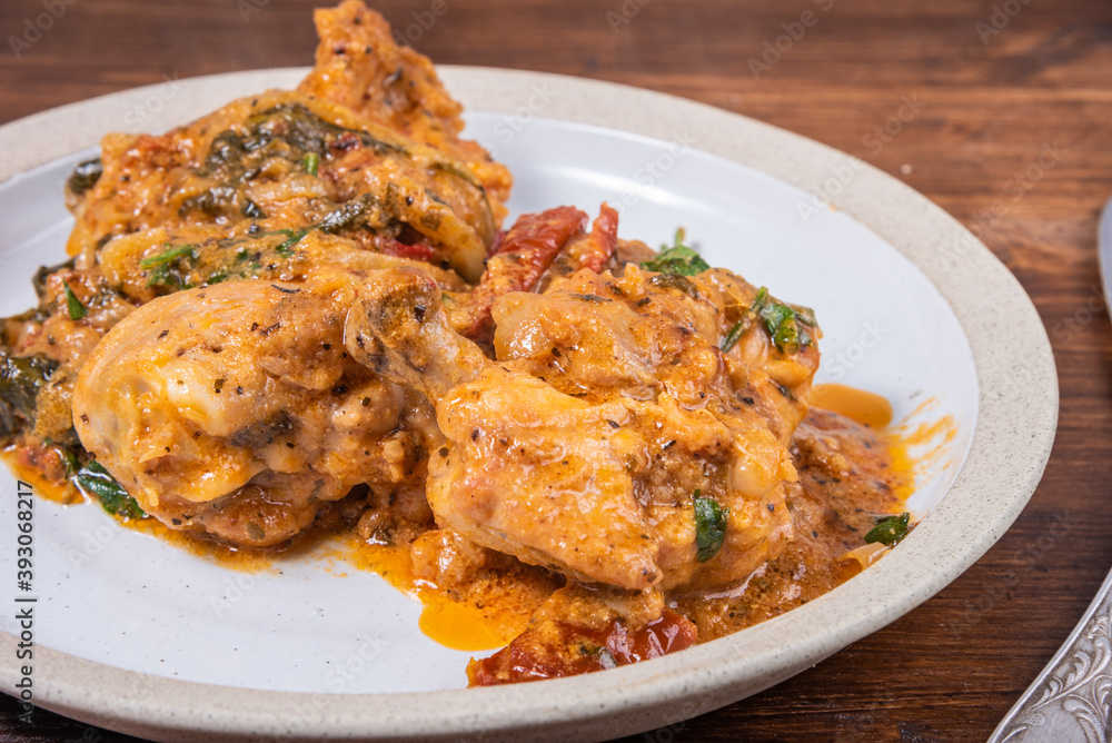 Ready Italian dish - Tuscan chicken with sun-dried tomatoes, tomato paste, spinach, cream and cheese on a plate on a wooden table Ready Italian dish - Tuscan chicken with sun-dried tomatoes, tomato paste, spinach, cream and cheese on a plate on a wooden table