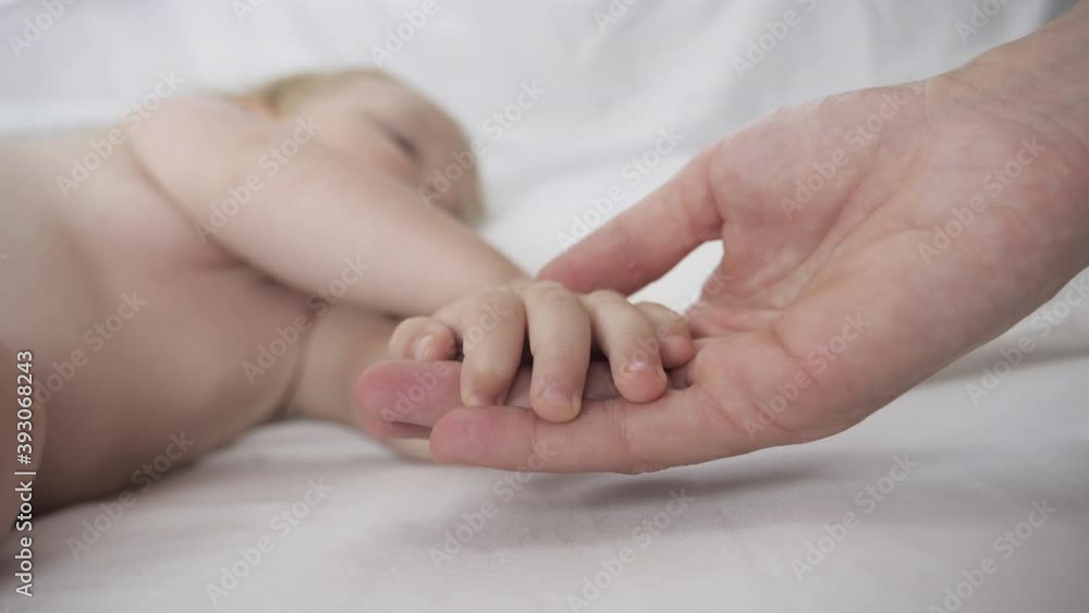 Newborn baby sleeping sweetly in a comfortable bed. Mom holds her baby's hand. Close up view, handheld shot, selective soft focus Newborn baby sleeping sweetly in a comfortable bed. Mom holds her baby's hand. Close up view, handheld shot, selective soft focus