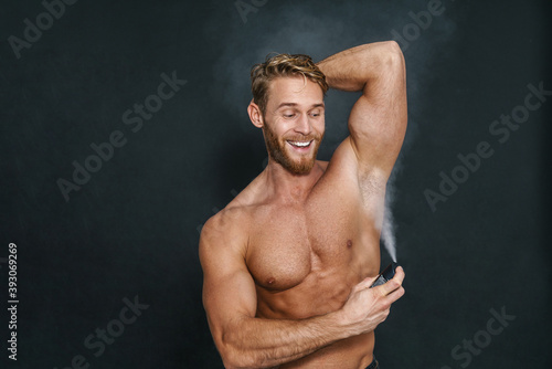 Happy caucasian shirtless man smiling while using deodorant
