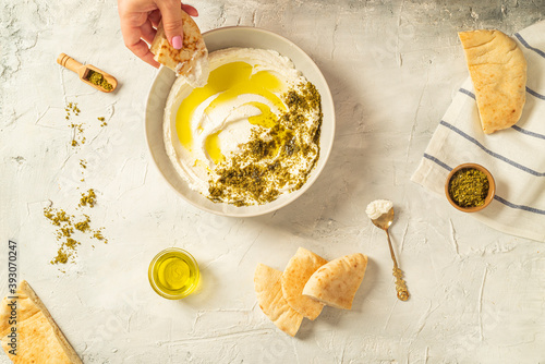 Popular middle eastern appetizer labneh or labaneh, soft white goat milk cheese with olive oil, hyssop or zaatar, served with pita bread over grey table, flaylay.