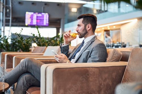 Adult man tasting some whisky with ice while tapping the phone