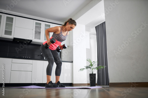 Fit young woman training back at home using weights.