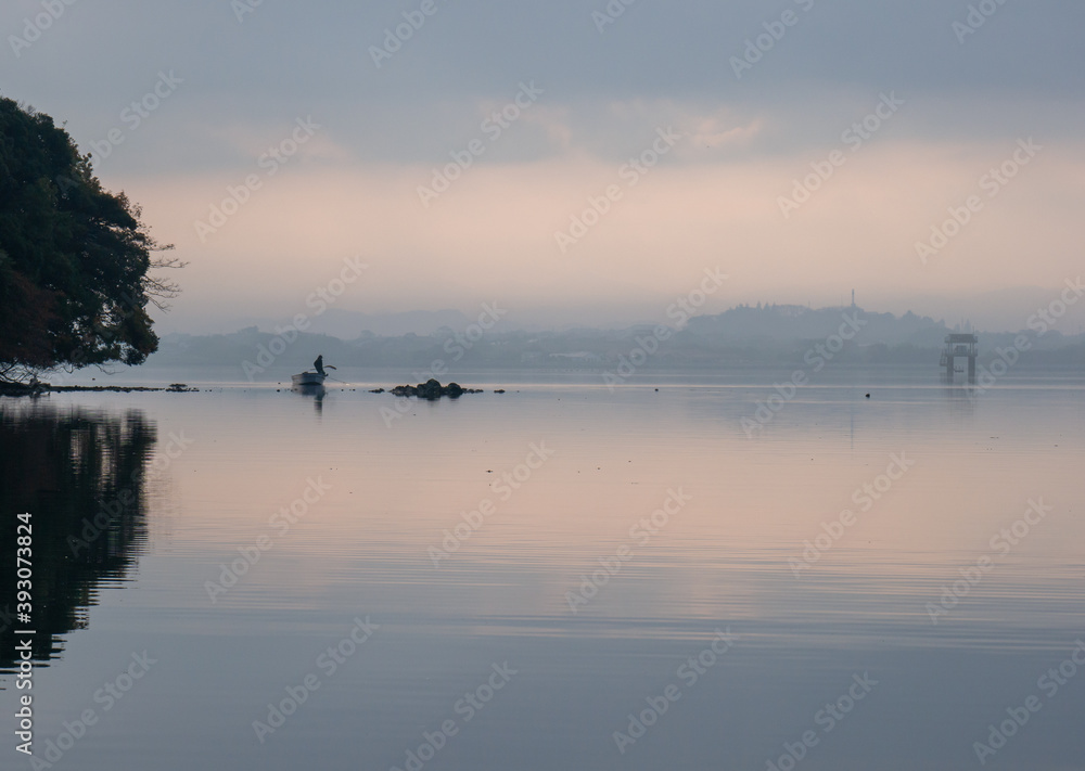 朝靄漂う海　小舟の上で網を引く男性