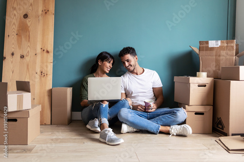 Attractive young couple looking decoration ideas with laptop while taking a break sitting on the floor at home. photo