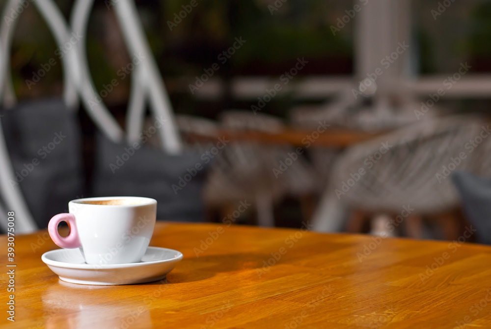 White coffee cup on a wooden board. Blurred bar interior on background. Free space near the coffee.