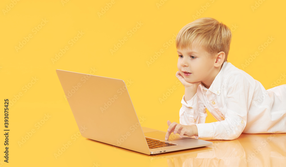 Litttle child boy using laptop on yellow background. Education, online study, home studying, distance learning. Primary school student during quarantine Litttle child boy using laptop on yellow background. Education, online study, home studying, distance learning. Primary school student during quarantine