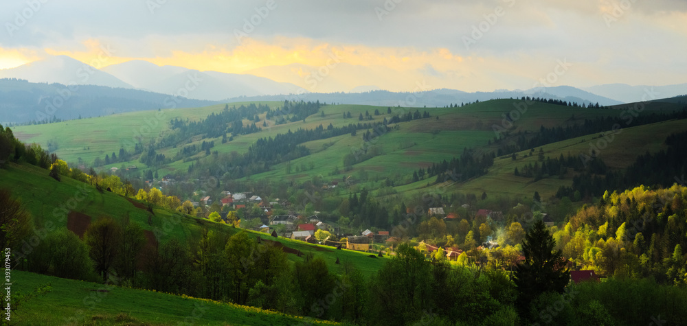 Spring morning rural landscape in the Carpathian mountains. Dramatic sky before dawn, ray of sun trying to break through the clouds.