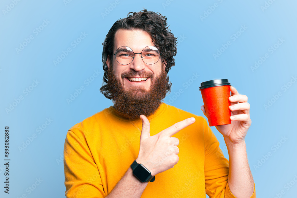 Cheerful bearded hipster man pointing at cup of coffee to Take Away.