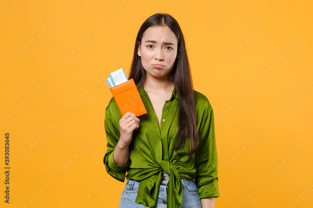 Upset traveler tourist asian woman in green shirt hold passport tickets isolated on yellow background, studio portrait. Passenger traveling abroad on weekends getaway. Air flight journey concept. Upset traveler tourist asian woman in green shirt hold passport tickets isolated on yellow background, studio portrait. Passenger traveling abroad on weekends getaway. Air flight journey concept.