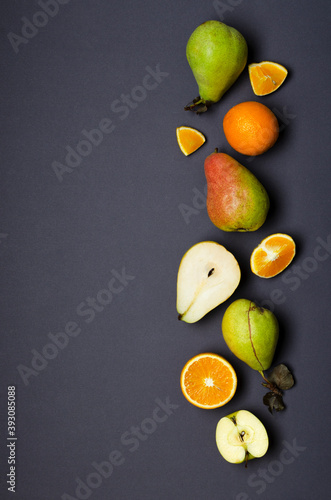 Top view of whole and pieces of oranges, pear, apples on the dark grey surface.Empty space