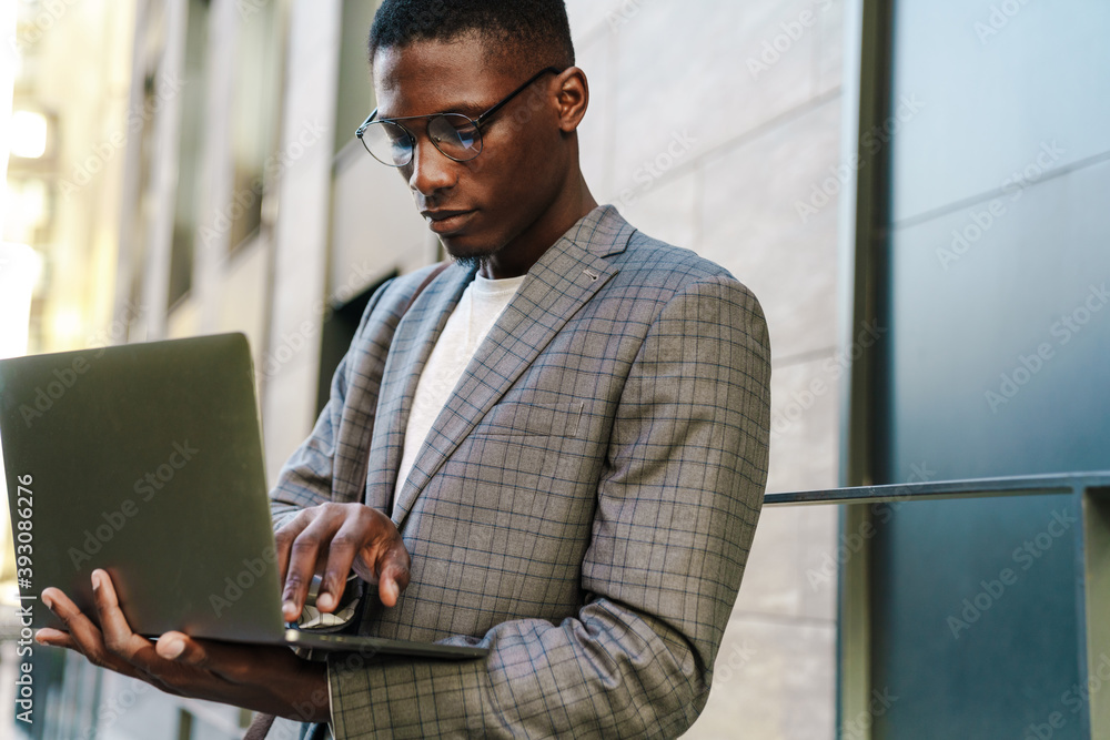 Focused african american man smiling and using laptop Focused african american man smiling and using laptop