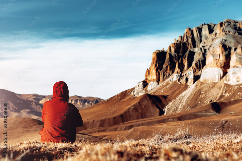 Woman in red jacket sitting alone in the mountains in Russia North Caucasus enjoying landscape. Travel lifestyle vacations tourism outdoor trip Back view - obrazy, fototapety, plakaty 