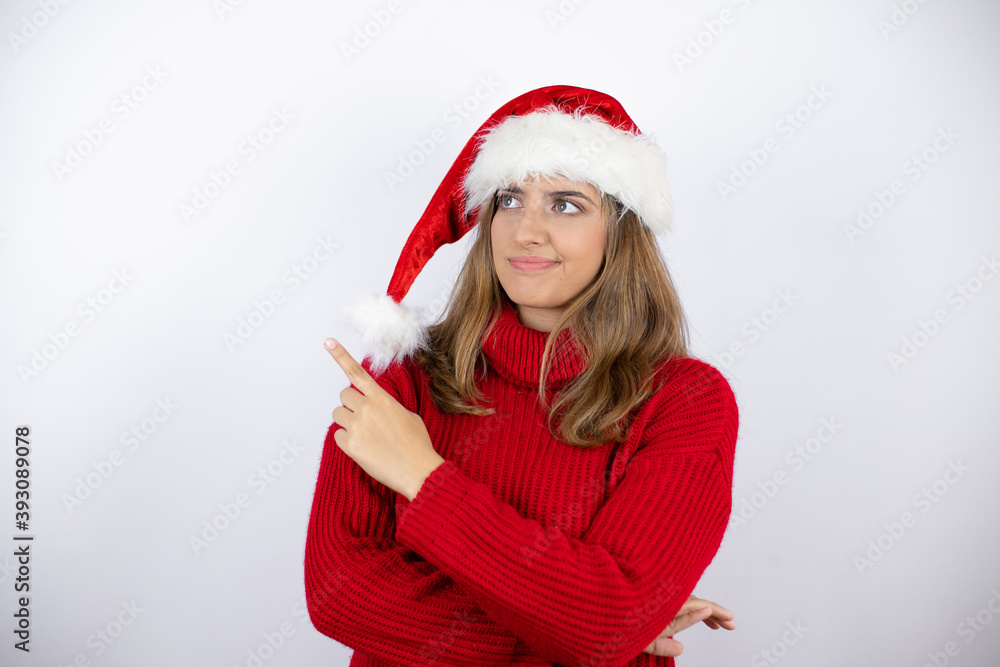 Young pretty blonde woman wearing a red casual sweater and a christmas hat over white background smiling happy pointing with hand and finger to the side Young pretty blonde woman wearing a red casual sweater and a christmas hat over white background smiling happy pointing with hand and finger to the side