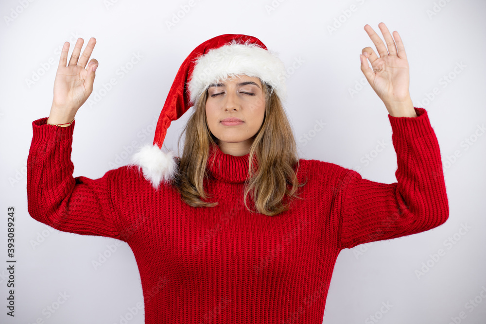 Young pretty blonde woman wearing a red casual sweater and a christmas hat over white background relax and smiling with eyes closed doing meditation gesture with fingers