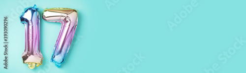 Creative layout. Rainbow foil balloon number, digit seventeen. Birthday greeting card with inscription 17. Anniversary concept. Top view. Stylish colored numeral on blue background. Numerical digit