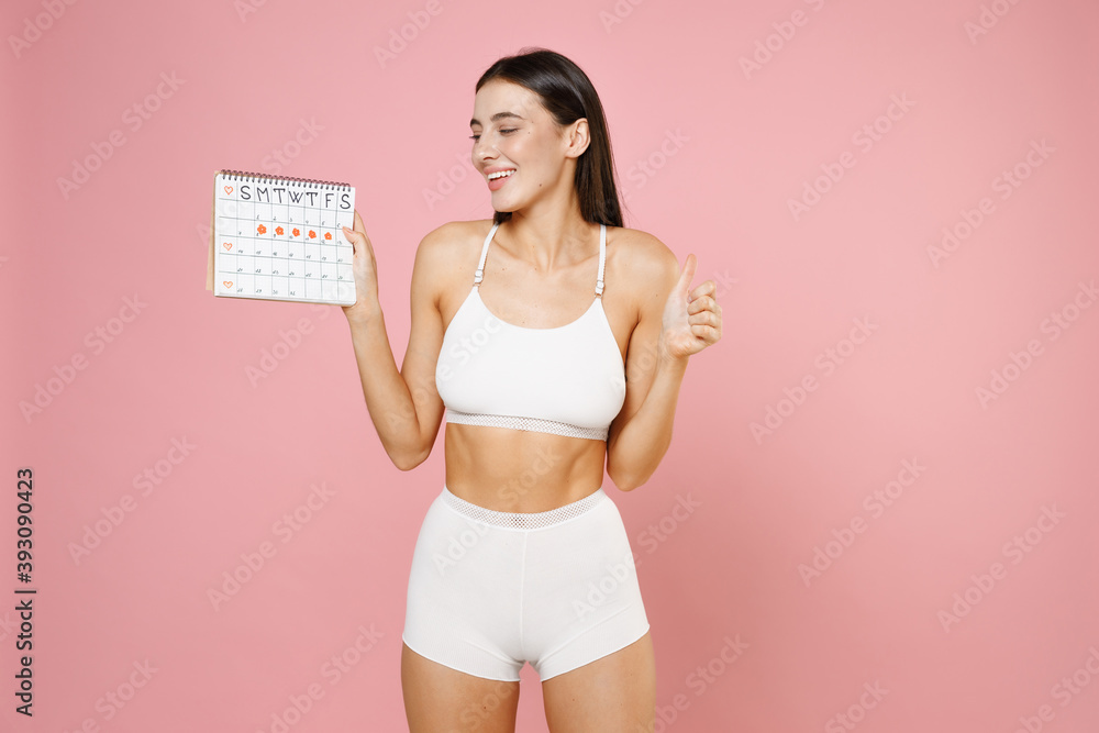 Naklejka premium Smiling young woman in underwear hold female periods calendar for checking menstruation days showing thumb up isolated on pink background, studio portrait. Medical, healthcare, gynecological concept.
