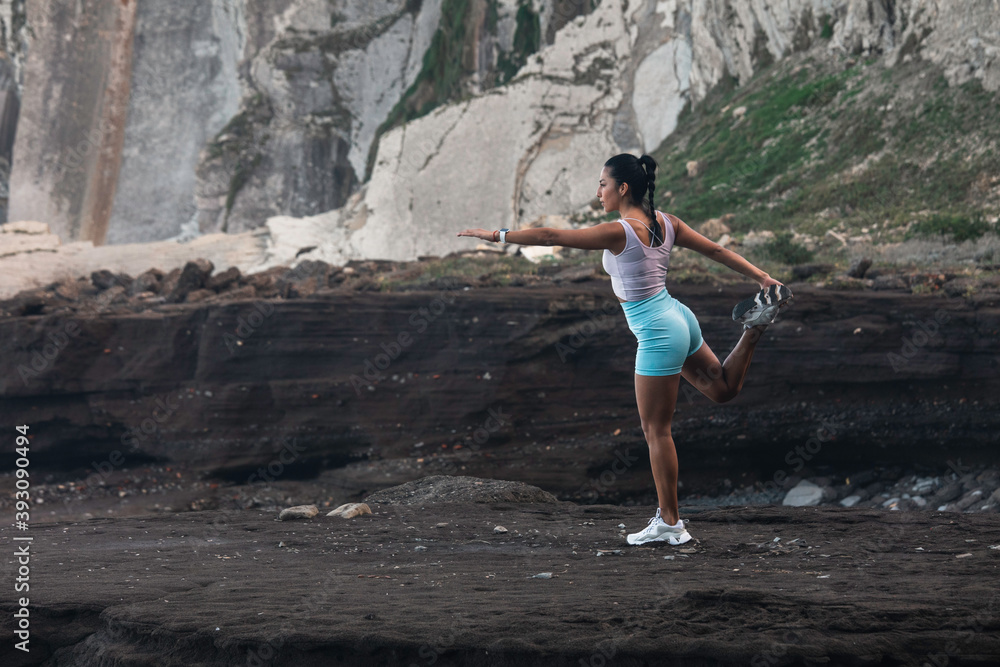Fototapeta premium young woman stretching before exercising while looking at the horizon on the beach