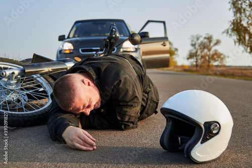 A motorcyclist lies on the asphalt near a motorcycle and car.