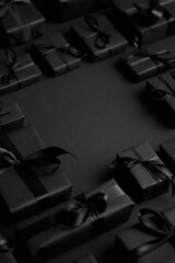 Arranged Gifts boxes wrapped in black paper with black ribbon on black background. Christmas concept