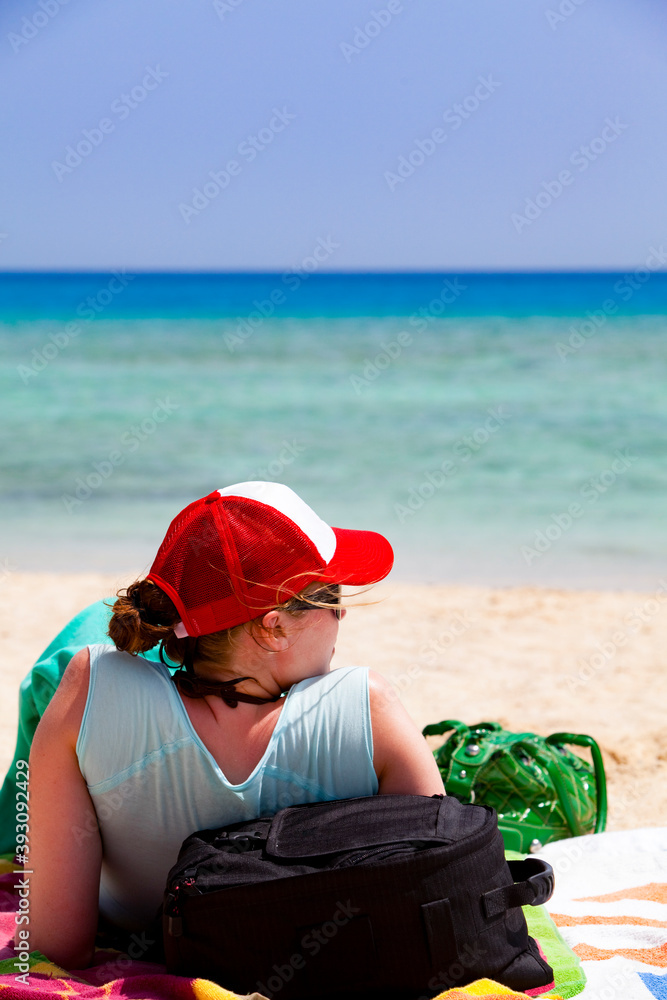 Young woman in with red cap relaxing on the beach on a sunny day.