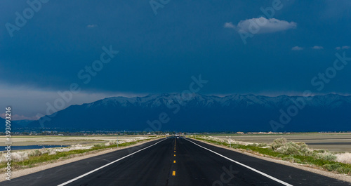 Straight road going towards a very stormy and black sky with the mountains on the horizon under heavy rain.  Angtelope island, Utah, United States of America photo