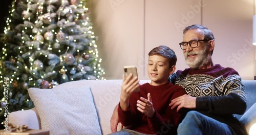 Wallpaper Mural Portrait of happy smiling Caucasian old grandpa with teen grandchild sitting in decorated room and taking selfie photos on smartphone at home near glowing new year tree. Christmas holidays concept Torontodigital.ca