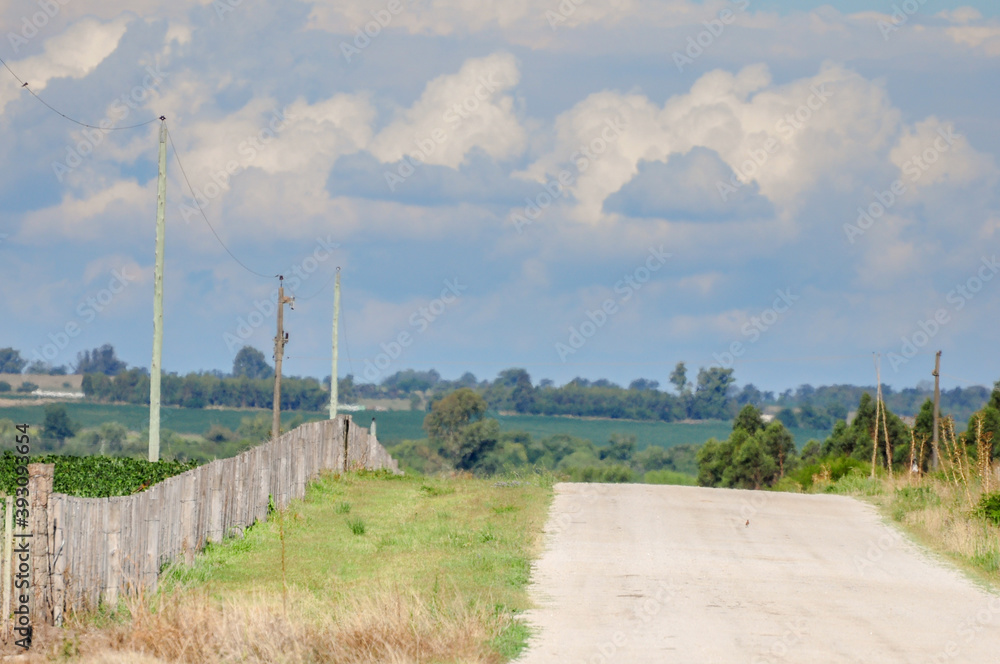 Lonely gravel road with a fence on the left side and a horizon full of stormy clouds