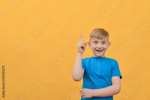 The boy on a yellow background shows thumbs up and looks at the camera.