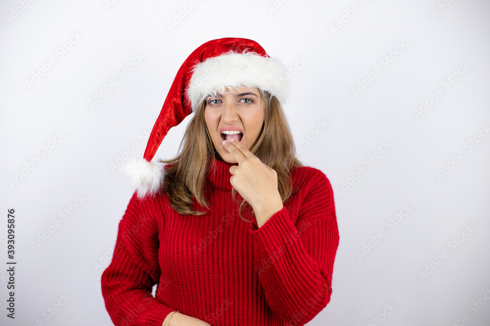 Young pretty blonde woman wearing a red casual sweater and a christmas hat over white background disgusted with her hand inside her mouth Young pretty blonde woman wearing a red casual sweater and a christmas hat over white background disgusted with her hand inside her mouth