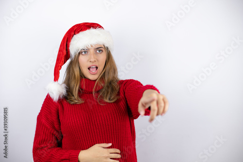 Young pretty blonde woman wearing a red casual sweater and a christmas hat over white background pointing with finger surprised ahead  open mouth amazed expression  something on the front