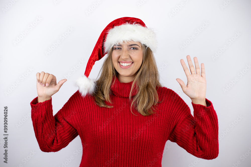Young pretty blonde woman wearing a red casual sweater and a christmas hat over white background showing and pointing up with fingers number six while smiling confident and happy Young pretty blonde woman wearing a red casual sweater and a christmas hat over white background showing and pointing up with fingers number six while smiling confident and happy