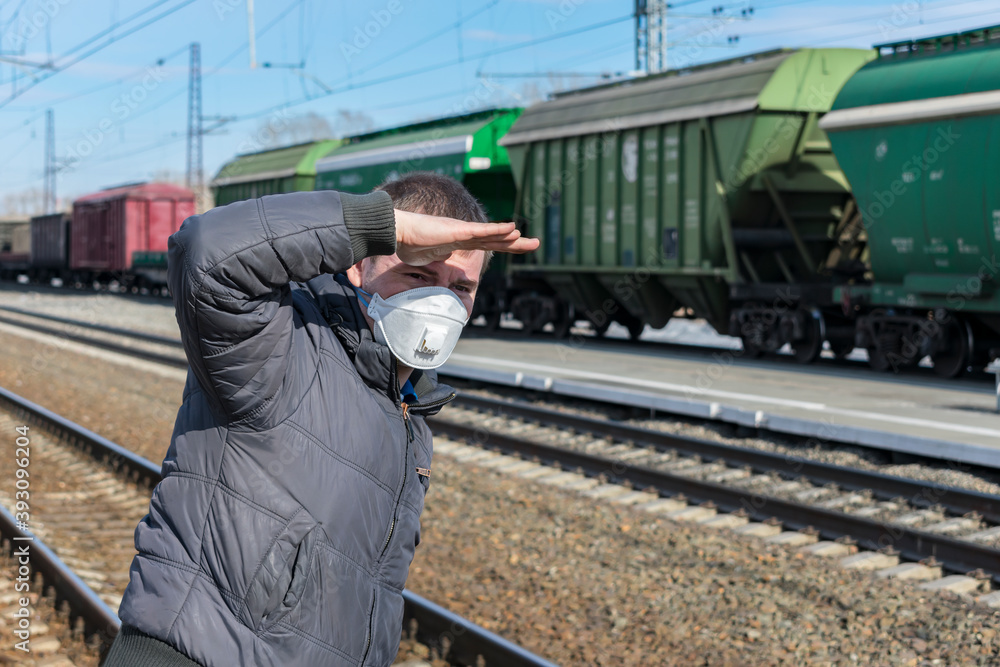 Man at the railway station waiting for his train, covering his face with his hand from the sun