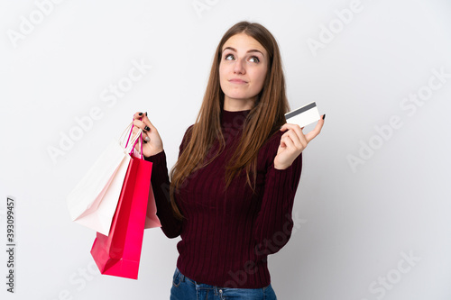 Young woman over isolated white background holding shopping bags and a credit card and thinking