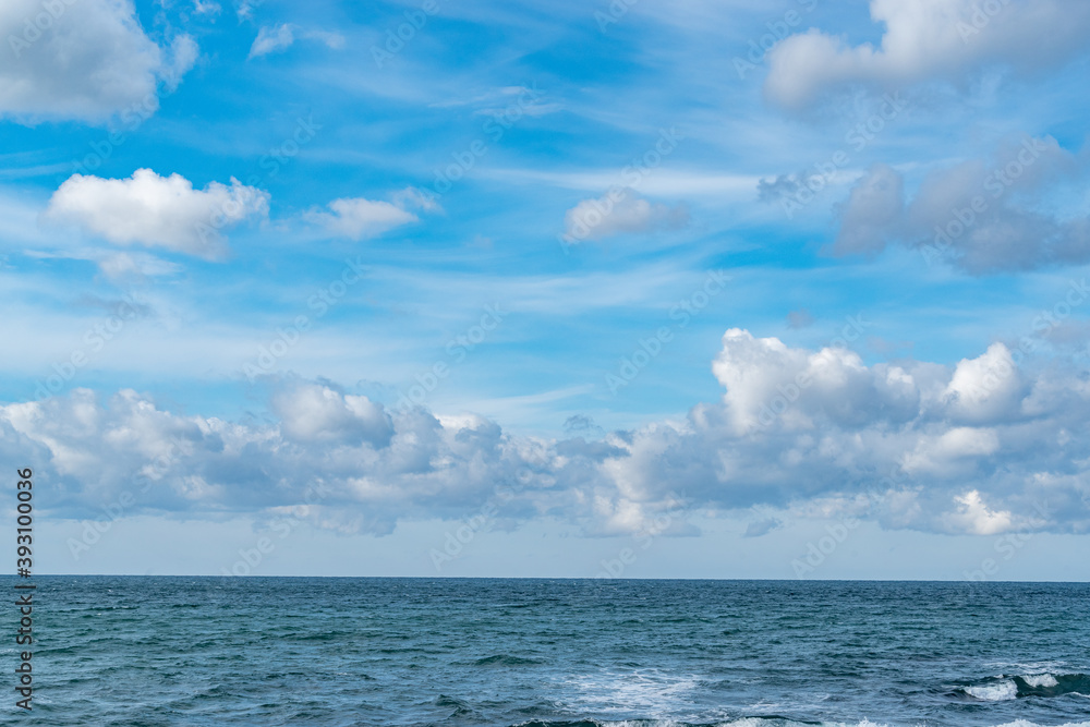 青空に浮かぶ雲とエメラルドグリーンの海の地平線