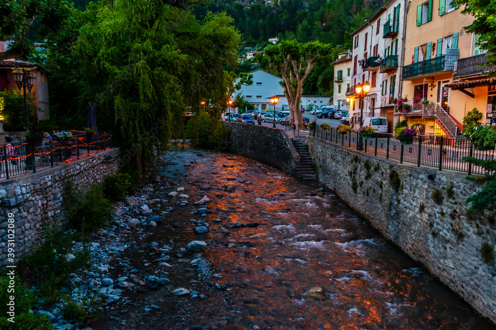 A picturesque view of a small mountain river flowing through a French medieval alpine village at dusk (Puget-Theniers, Alpes-Maritimes, Provence-Alpes-Cote-d'Azur, France)