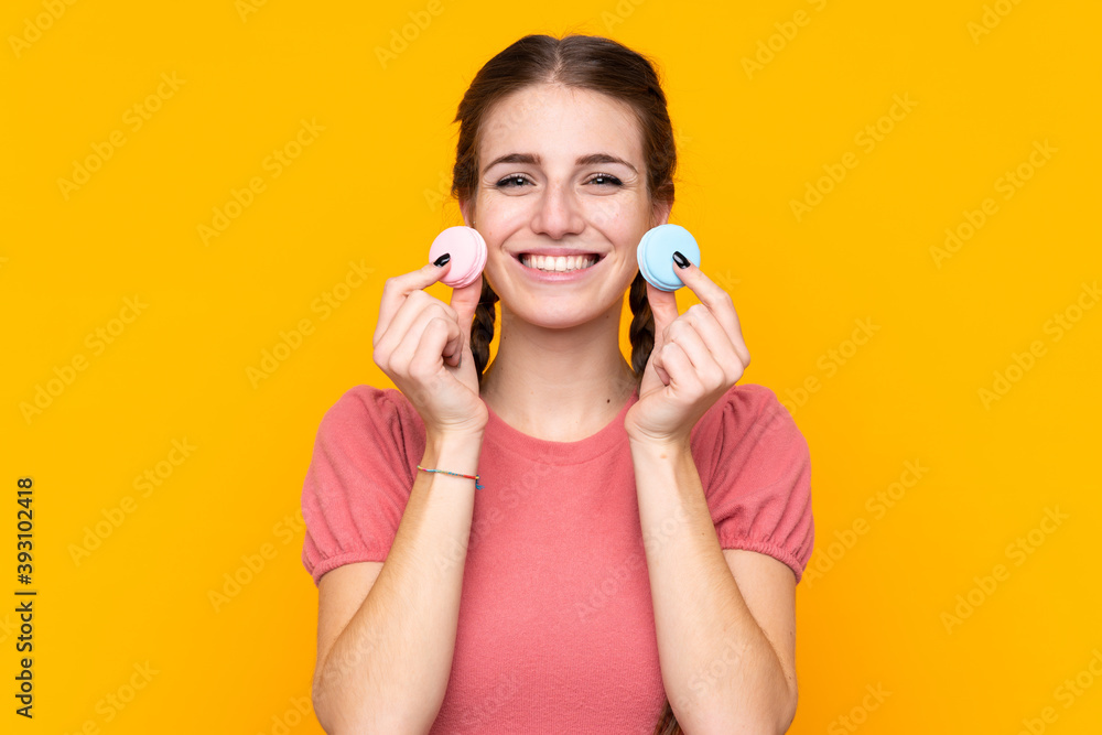 Young woman over isolated yellow background holding colorful French macarons and smiling Young woman over isolated yellow background holding colorful French macarons and smiling