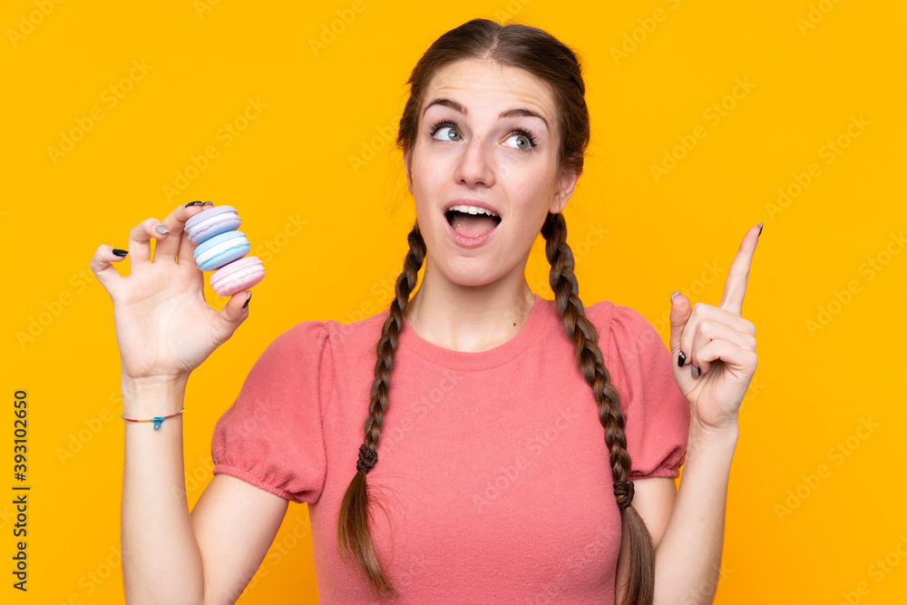 Young woman over isolated yellow background holding colorful French macarons and intending to realizes the solution Young woman over isolated yellow background holding colorful French macarons and intending to realizes the solution