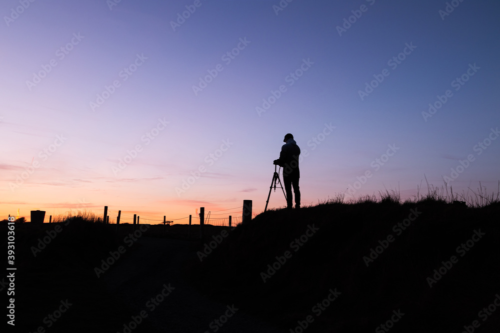 Silhouette of a person using a camera on a tripod